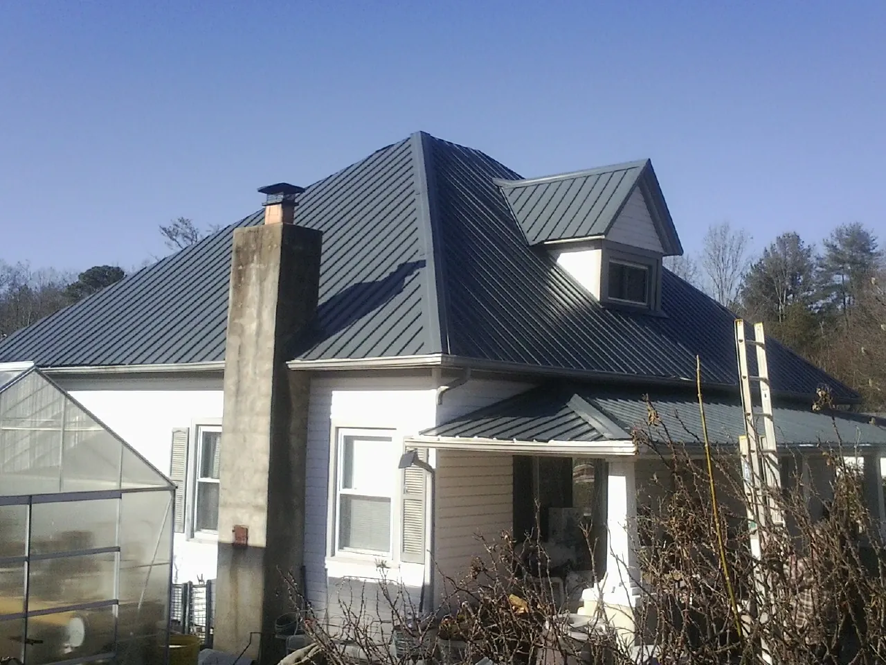 Dark blue standing seam metal roof on a white farmhouse with dormer — Slate & Tile Roof Repair by Roofing Brothers in College Station