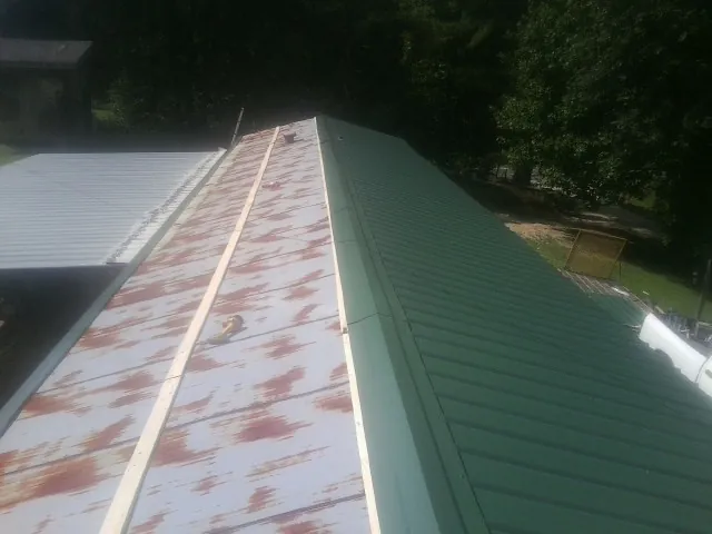 Old rusted panels beside newly installed green metal roofing — Wind Damage Roof Repair by Roofing Brothers in College Station
