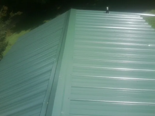 New green metal panels meeting at the ridge of a roof — Flat Roof Repair work by our crew in College Station