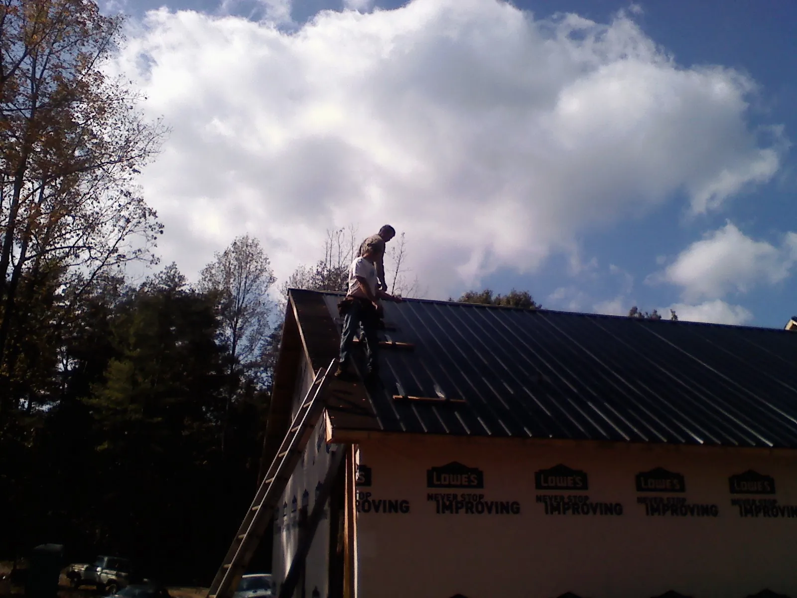 Roofer fastening dark metal panels high against a cloudy sky, from a Roof Inspection job in College Station