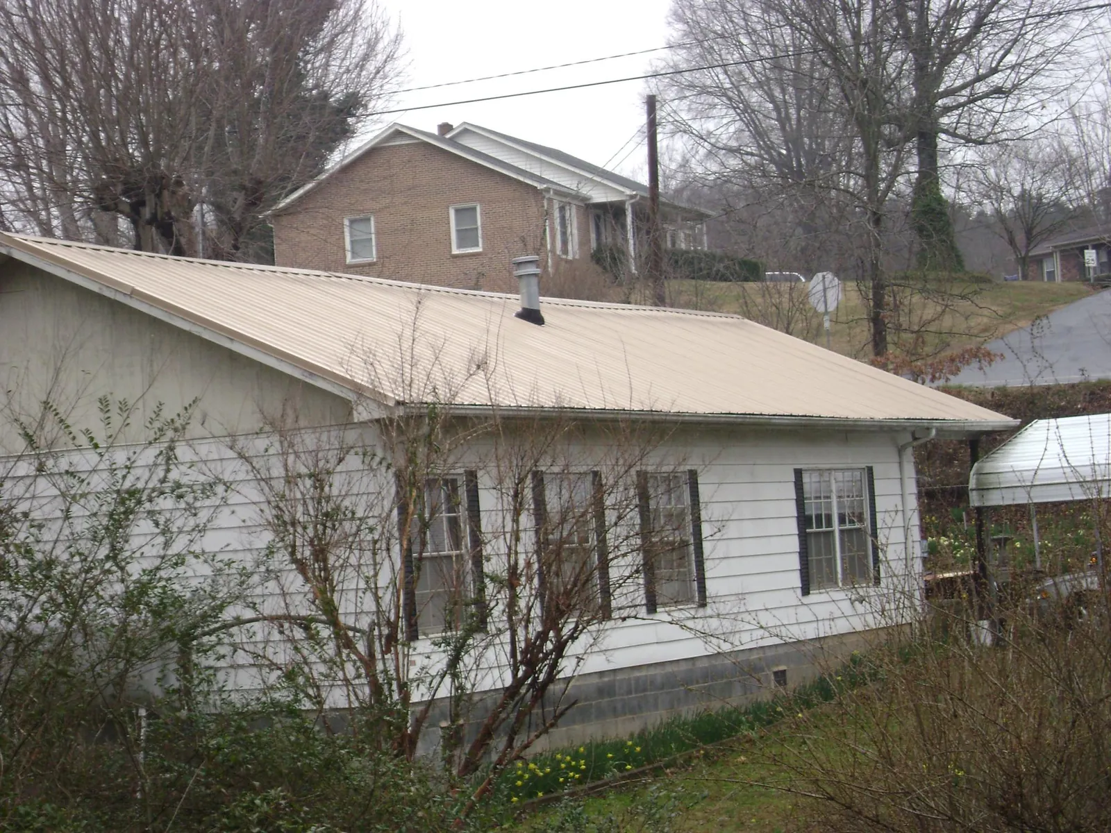 Tan metal roof on a white sided house set into a hillside — Commercial Roofing by Roofing Brothers in College Station