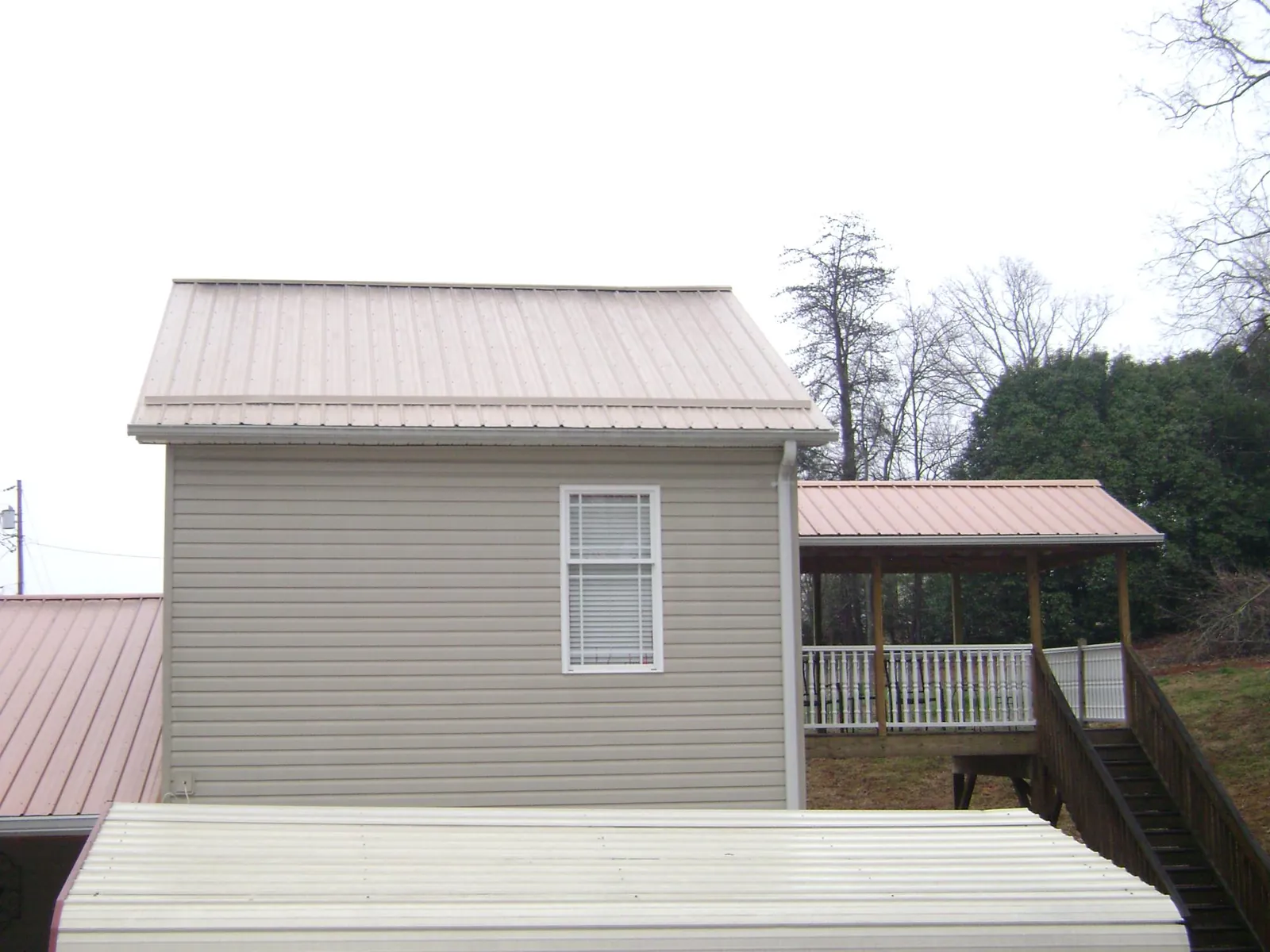 Tan metal roofs on a two story addition and attached porch, from a Roof Replacement job in College Station