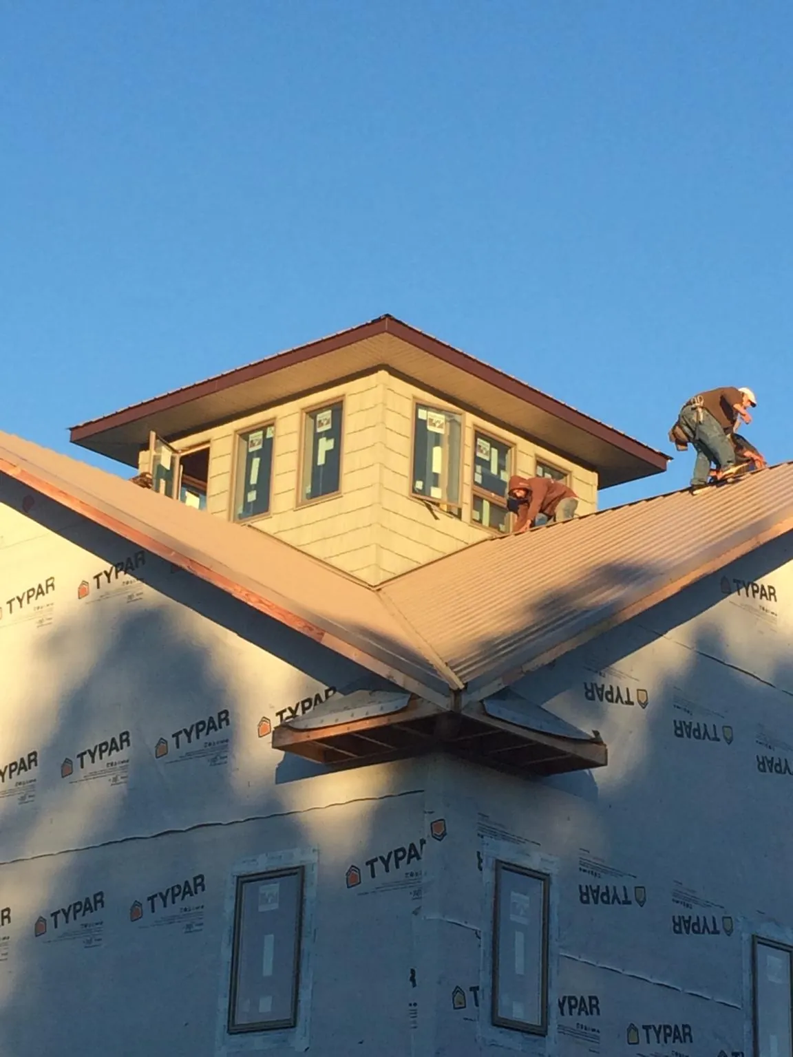 Roofers working around a rooftop cupola on a new metal roof at sunset — Roof Waterproofing in College Station by Roofing Brothers